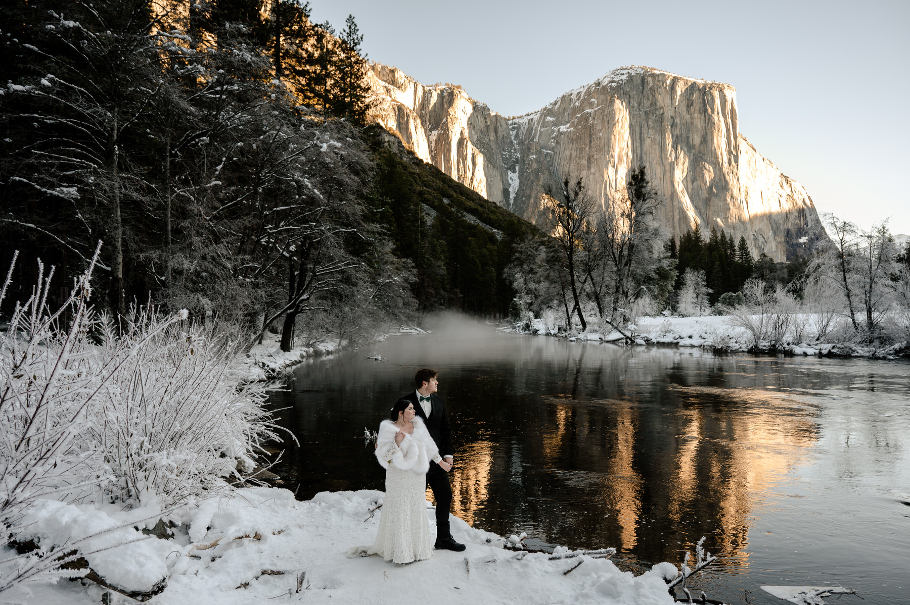 a bride and groom surrounded by snow with mountains in the background during their winter wedding in Yosemite