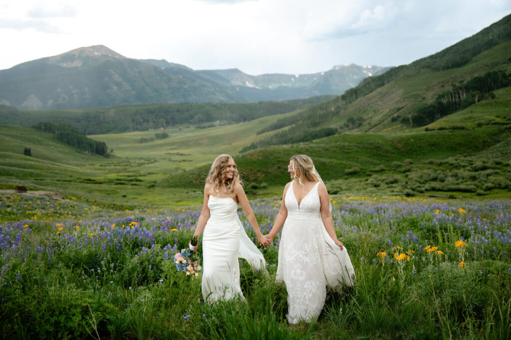 Two brides walking through flowers in the mountains on their wedding day
